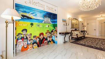 Una sala de reuniones con un mural, candelabros, un sofá y una alfombra estampada.