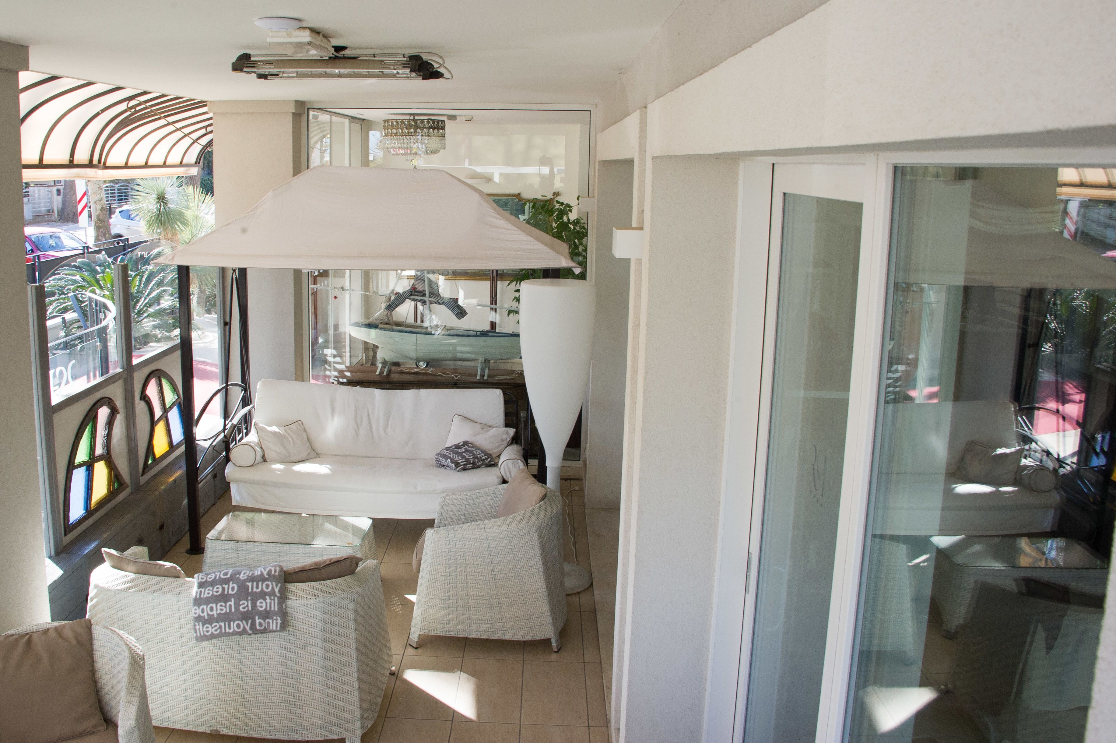 Una habitación iluminada por el sol con un sofá blanco, dos sillones de mimbre y un paraguas grande de color blanco.
