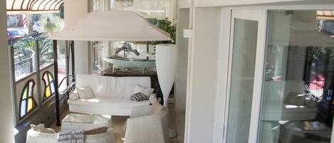 Et solbelyst rum med en hvid sofa, to fletstole og en stor, hvid parasol.