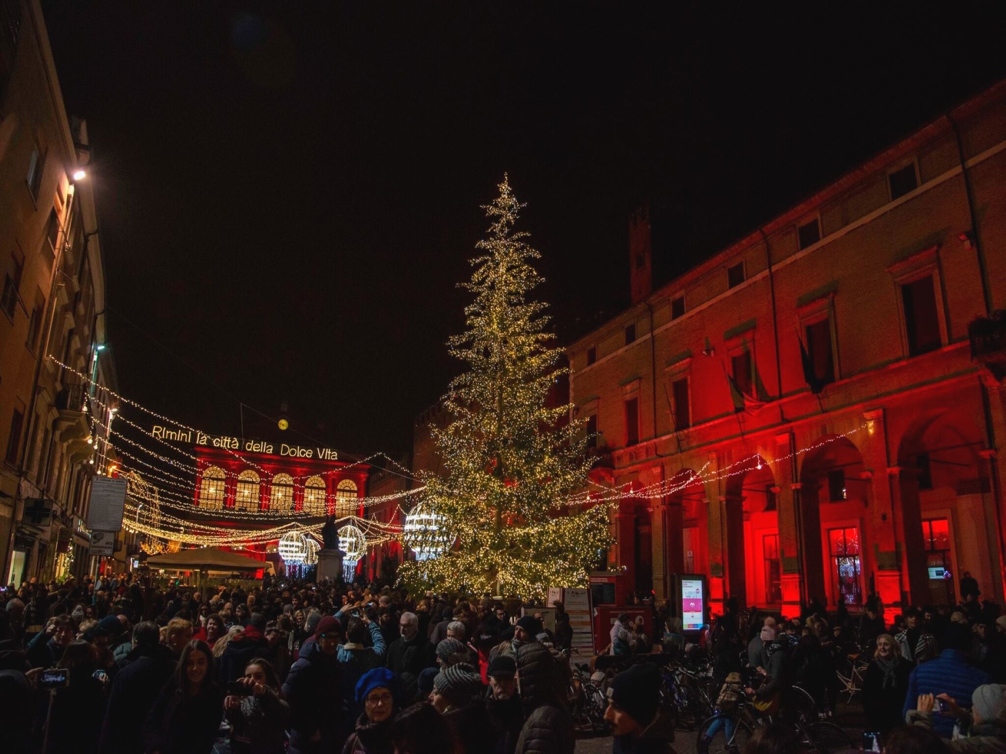 Una plaza concurrida con un gran árbol de Navidad decorado y edificios iluminados.