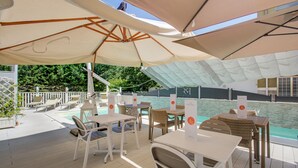 Un área de estar al aire libre con mesas y sillas bajo grandes sombrillas, con vista a una piscina.