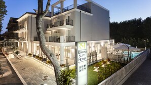 Un hotel moderno con varios balcones, una piscina y una entrada bien iluminada.