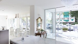 Un comedor luminoso y moderno con mobiliario blanco, una lámpara de araña grande y vista a la calle.