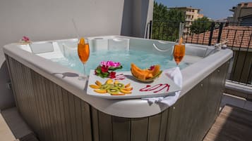 A hot tub with a tray of fruit and drinks, surrounded by a wooden deck and a balcony railing.