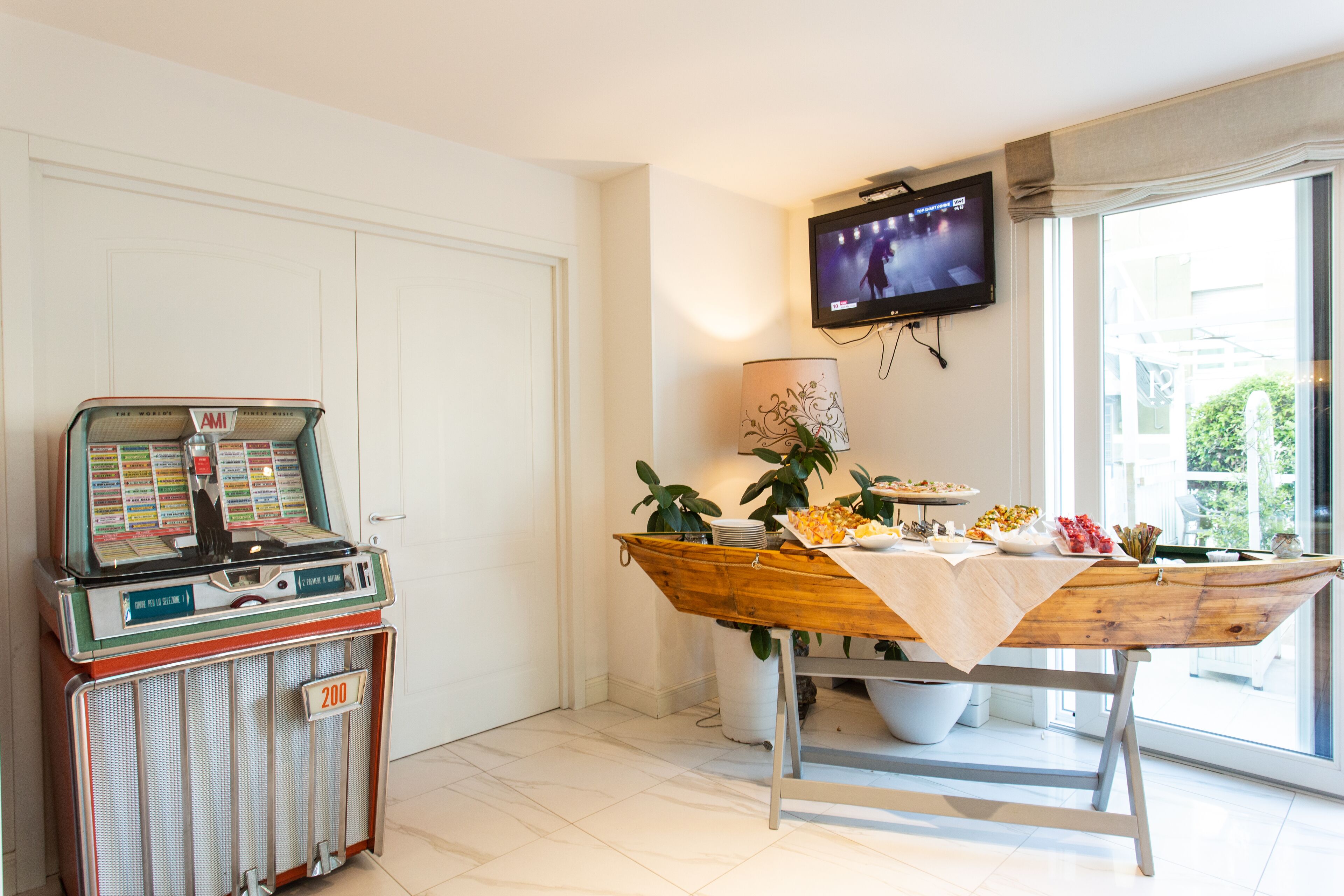Una habitación con un radiola, una mesa con comida, un televisor y un ventanal con vistas.