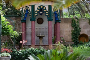 A traditional fountain with a decorative arch and a tiled base, surrounded by lush greenery and flowering plants. - Hotel S'Ardeviu (Sóller)