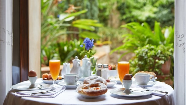 Una mesa de desayuno con pasteles, huevos y jugo de naranja, con vistas a un jardín exuberante.