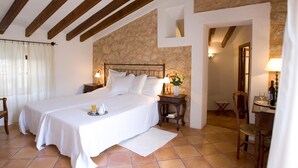 Un dormitorio con una cama grande, vigas de madera, pared de piedra y una mesita con una lámpara y flores.