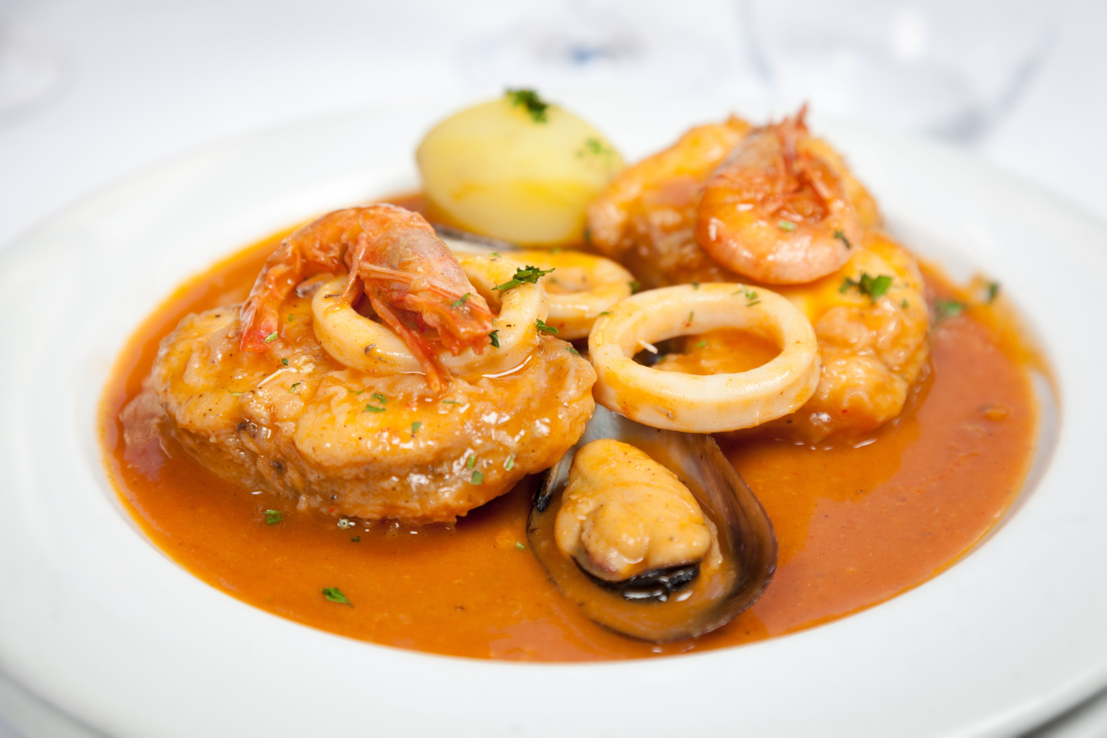 A seafood dish with shrimp, mussels, and squid in a tomato-based sauce, served with a boiled potato.