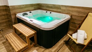 A corner room with a wooden bench, a chair with a towel, and a hot tub. - Hotel El Guía (Sóller)