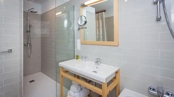 A modern bathroom with a glass-enclosed shower, a white sink with a mirror above, and a wooden vanity.
