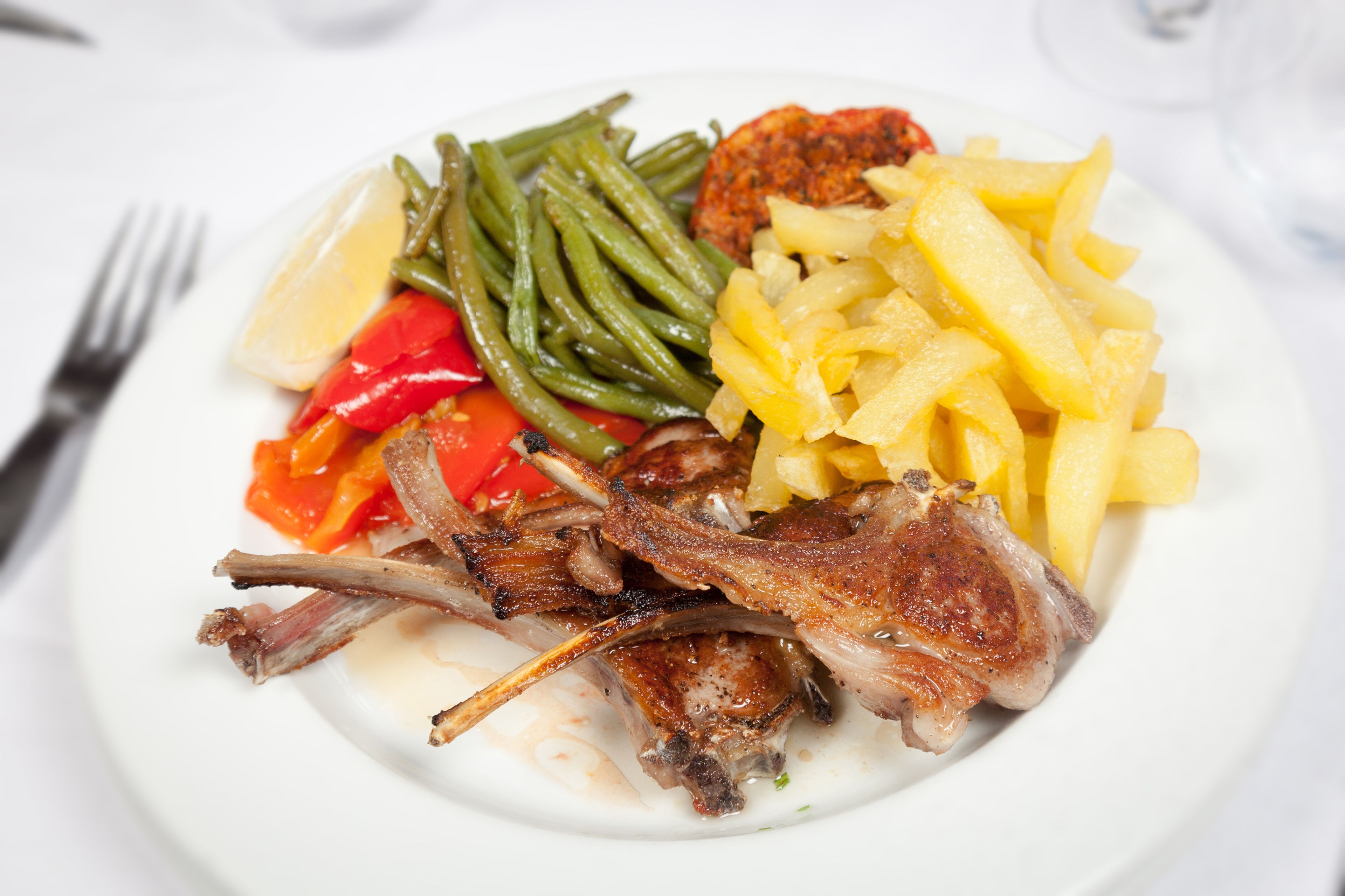 A plate of food including roasted meat, green beans, red peppers, and potatoes.