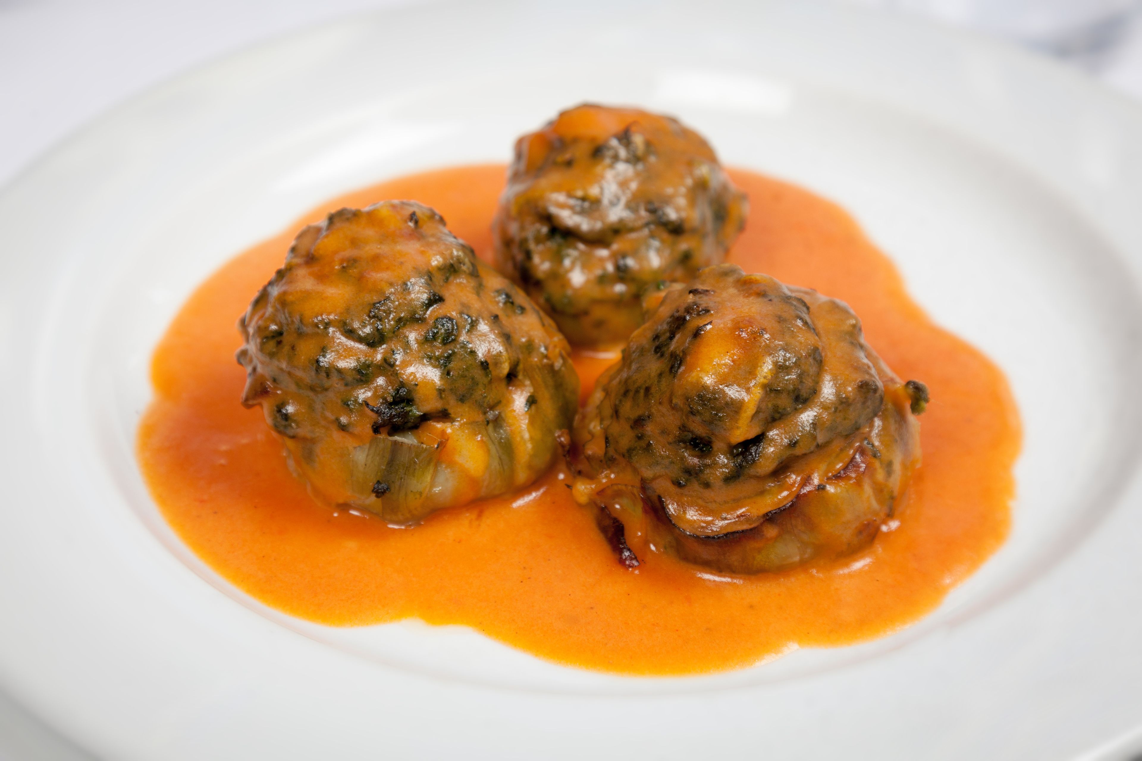 Three stuffed mushrooms with a tomato-based sauce on a white plate.