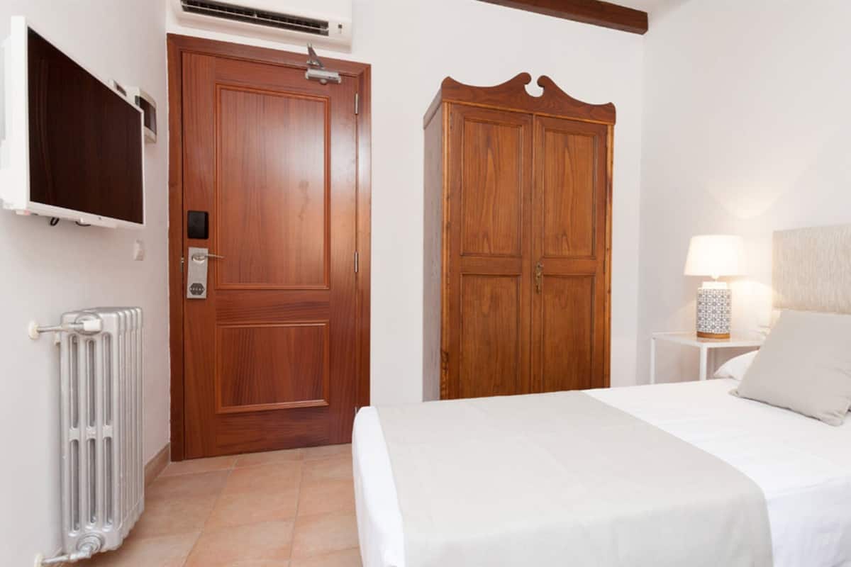 A bedroom with a bed, a wardrobe, a radiator, and a TV mounted on the wall.