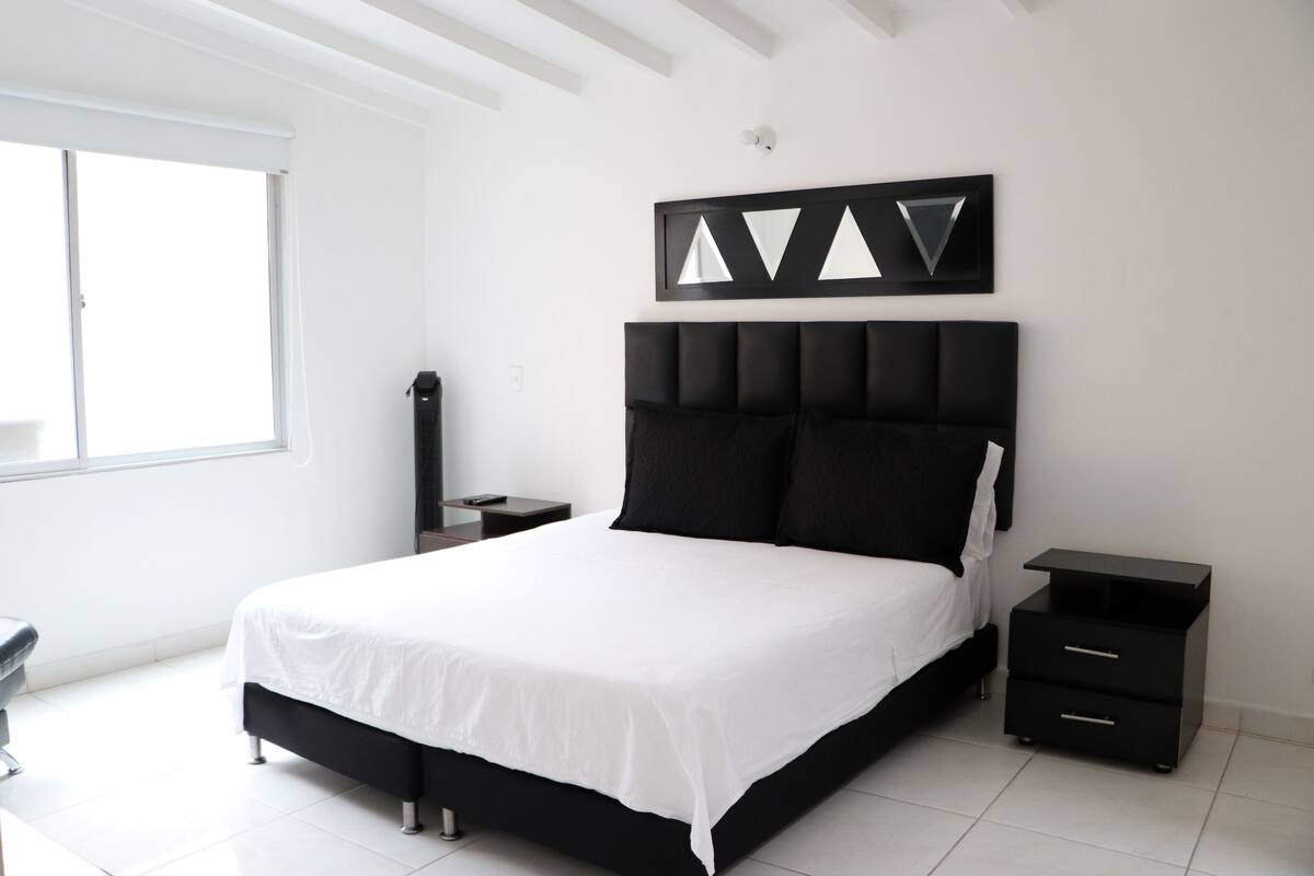 A modern bedroom with a large bed, a nightstand, a chair, and a window.