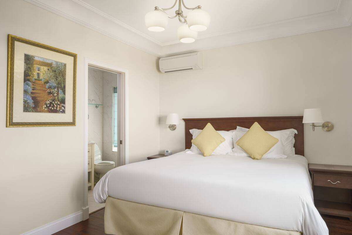 A neatly arranged bedroom with a large bed, bedside tables, a wall-mounted air conditioner, and a framed picture on the wall.