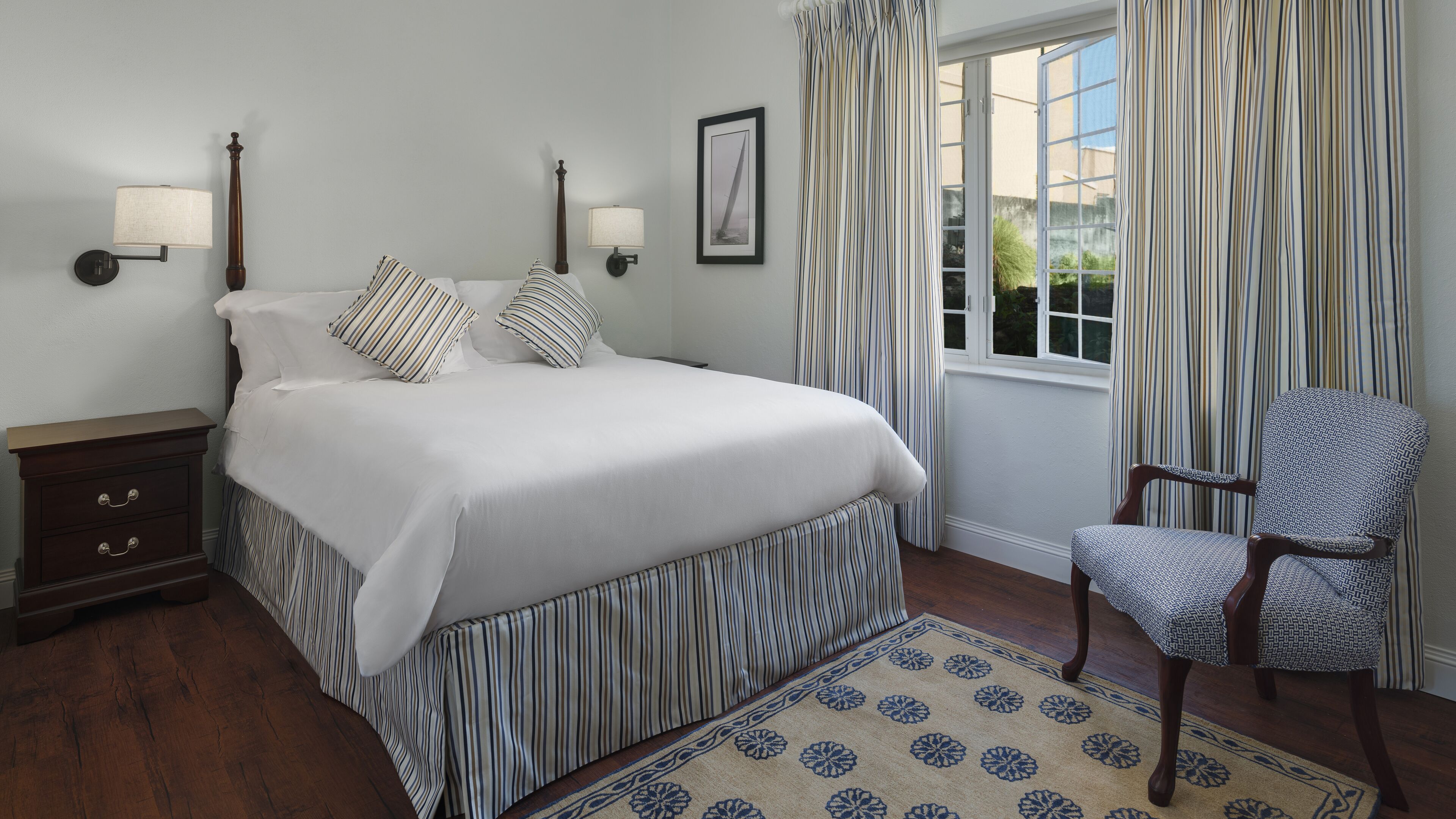 A neatly arranged bedroom with a large bed, two bedside tables, a chair, and a window with curtains.