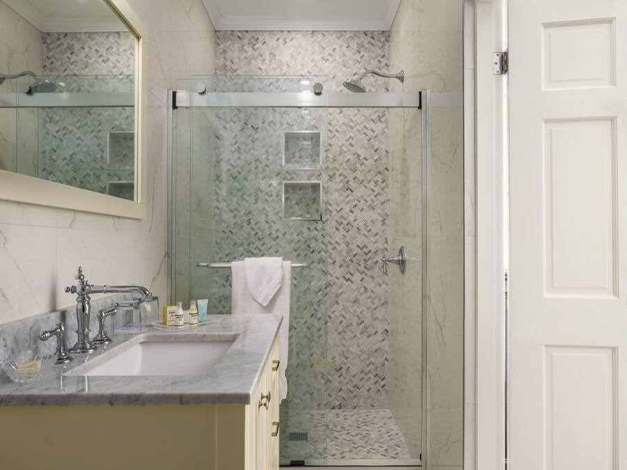 Un baño con lavamanos de mármol, cabina de ducha con mampara de vidrio y puerta blanca.