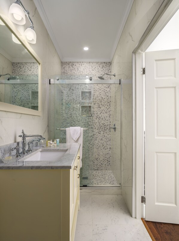A bathroom with a marble sink, a glass shower enclosure, and a white door.