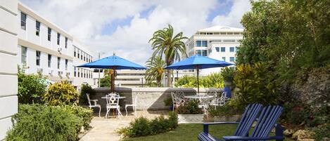 Un espace patio avec des sièges d’extérieur, comprenant une chaise Adirondack bleue et des chaises blanches, placés sous des parasols bleus.