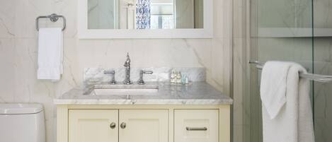 A bathroom with a marble-tiled wall, a glass shower enclosure, a vanity with a mirror, and a towel rack.