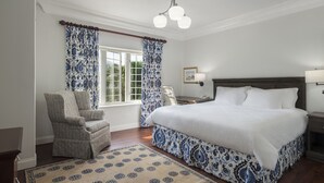 A bedroom with a large bed, a chair, a nightstand, a lamp, and a window with curtains. - The Oxford House (Pembroke Parish)