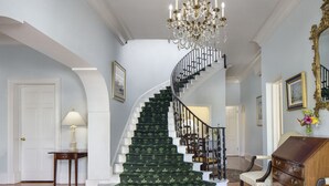 A grand staircase with a green carpet, a chandelier, and a wooden dresser. - The Oxford House (Pembroke Parish)