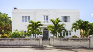A two-story white building with a central entrance, flanked by palm trees and a stone wall. - The Oxford House (Pembroke Parish)