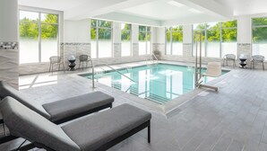 Ein moderner, überdachter Pool mit klaren Glaswänden, grauen Liegestühlen und Fliesenboden.