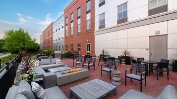 An outdoor patio area with seating, a fire feature, and a view of a building with a brick facade and large windows.