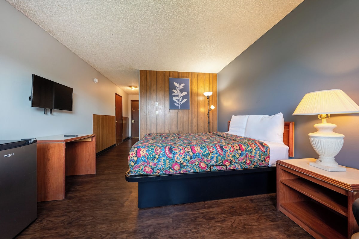 A hotel room with a bed, a desk, a TV, and a lamp.