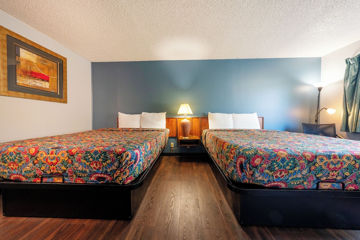A room with two beds, a nightstand with a lamp, and a framed picture on the wall.