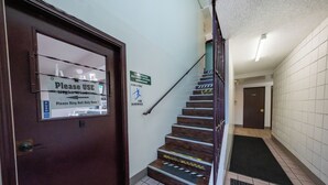 Un escalier muni de rampes, une porte avec une pancarte indiquant d’utiliser la guérite de nuit, et une autre pancarte conseillant de faire attention pour éviter une chute.