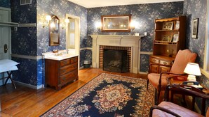 A room with a fireplace, wooden furniture, a patterned rug, and a mirror with wall sconces.