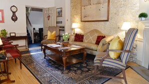 A cozy living room with a sofa, armchairs, a coffee table, and a rug. There is a staircase in the background leading to another floor.