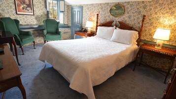 Un dormitorio ordenado con una cama grande, dos sillones, una mesa y una lámpara.