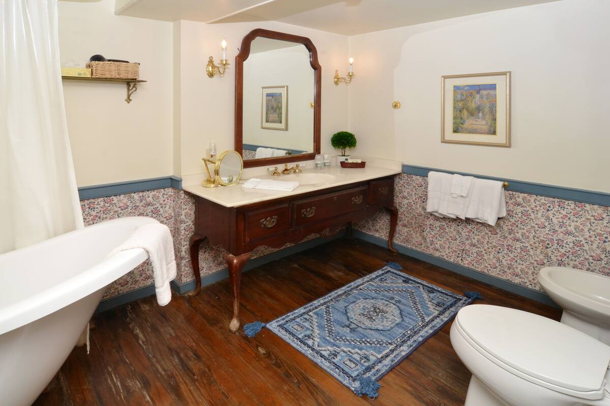 A bathroom with a bathtub, a sink, a mirror, a toilet, a rug, and a wall-mounted shelf.