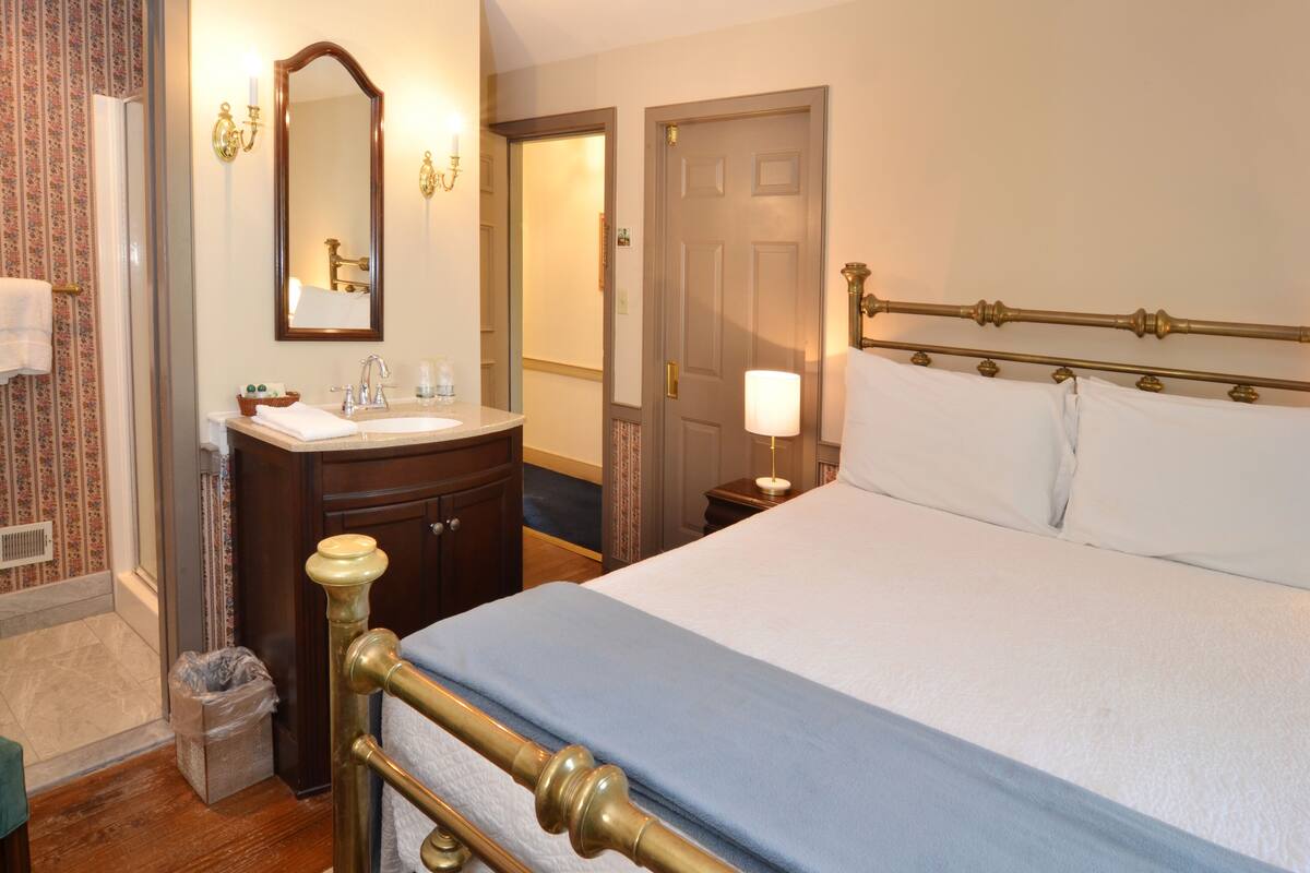 A hotel room with a bed, a bathroom with a sink and mirror, and a door leading to another room.