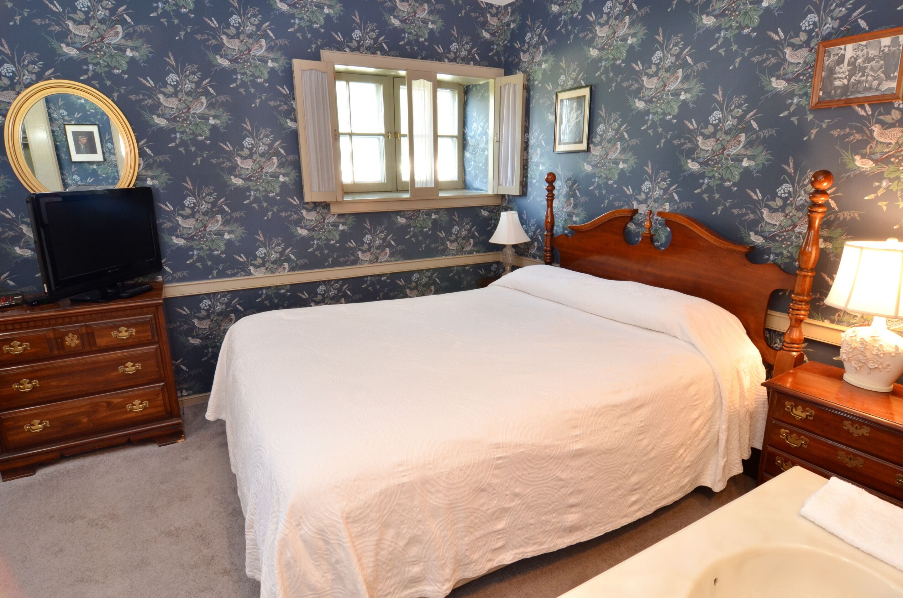 A bedroom with a bed, dresser, vanity, and a window with curtains.