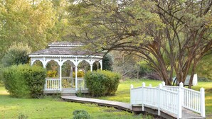 A gazebo with a white railing and a wooden bridge in a garden.