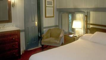 Une chambre d’hôtel avec un lit, une chaise, une table de chevet avec une lampe, une commode et une porte.
