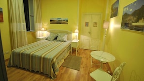 A bedroom with a bed, bedside tables, a chair, a small table, and a door. - Domus Ripetta (Rome)