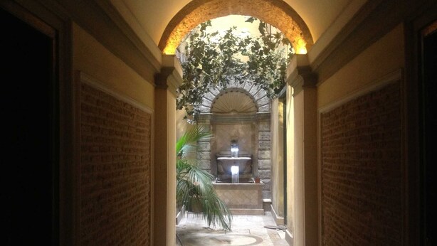 A corridor with a stone fountain, arched ceiling, and potted plants. - Domus Ripetta (Rome)