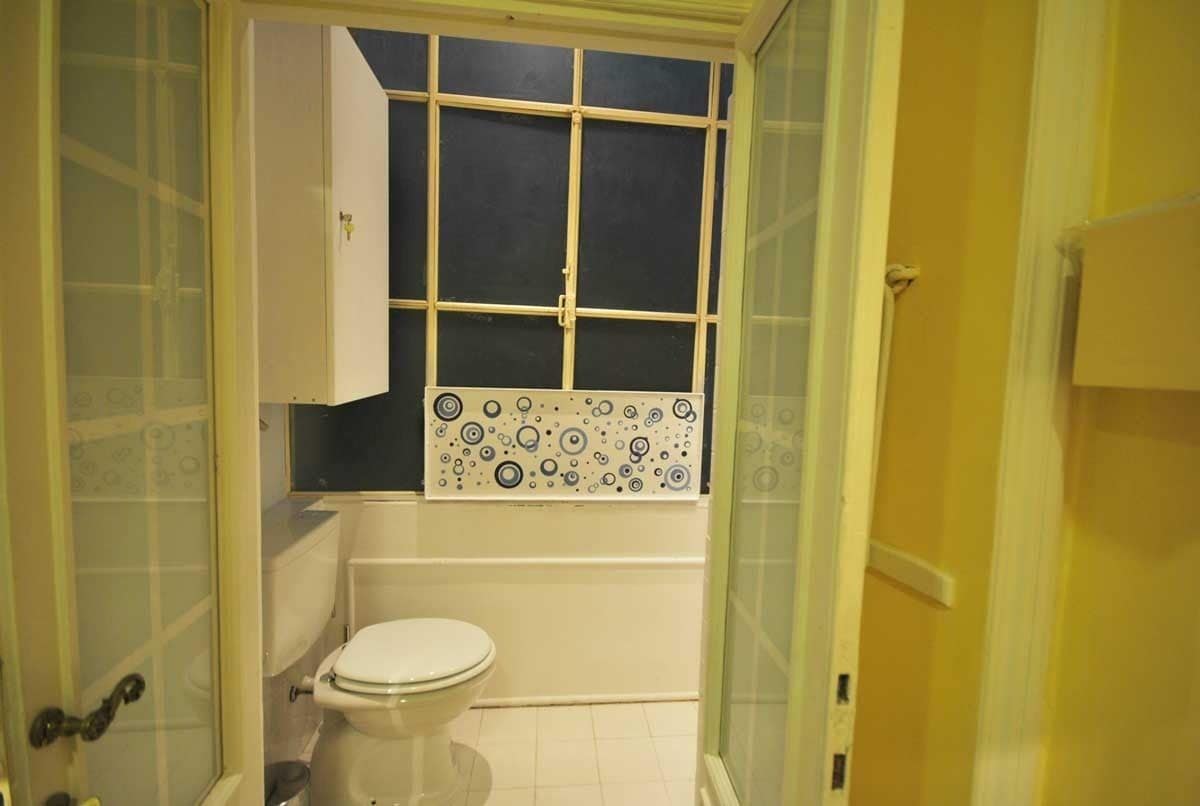 Un baño pequeño con inodoro, ventana con diseño de celosía y pared de azulejos.