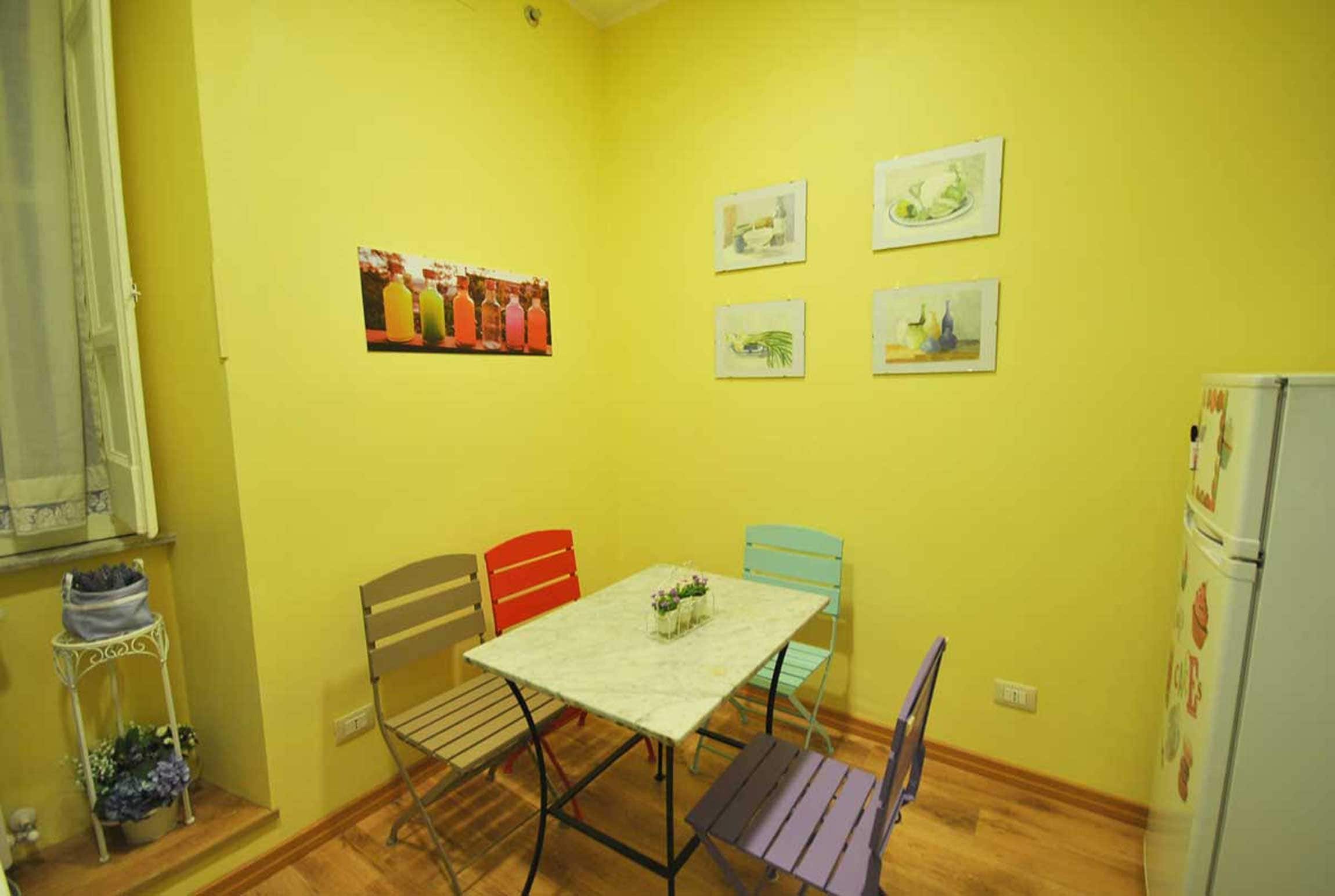 Un pequeño comedor con una mesa, sillas, un refrigerador y una estantería decorada.