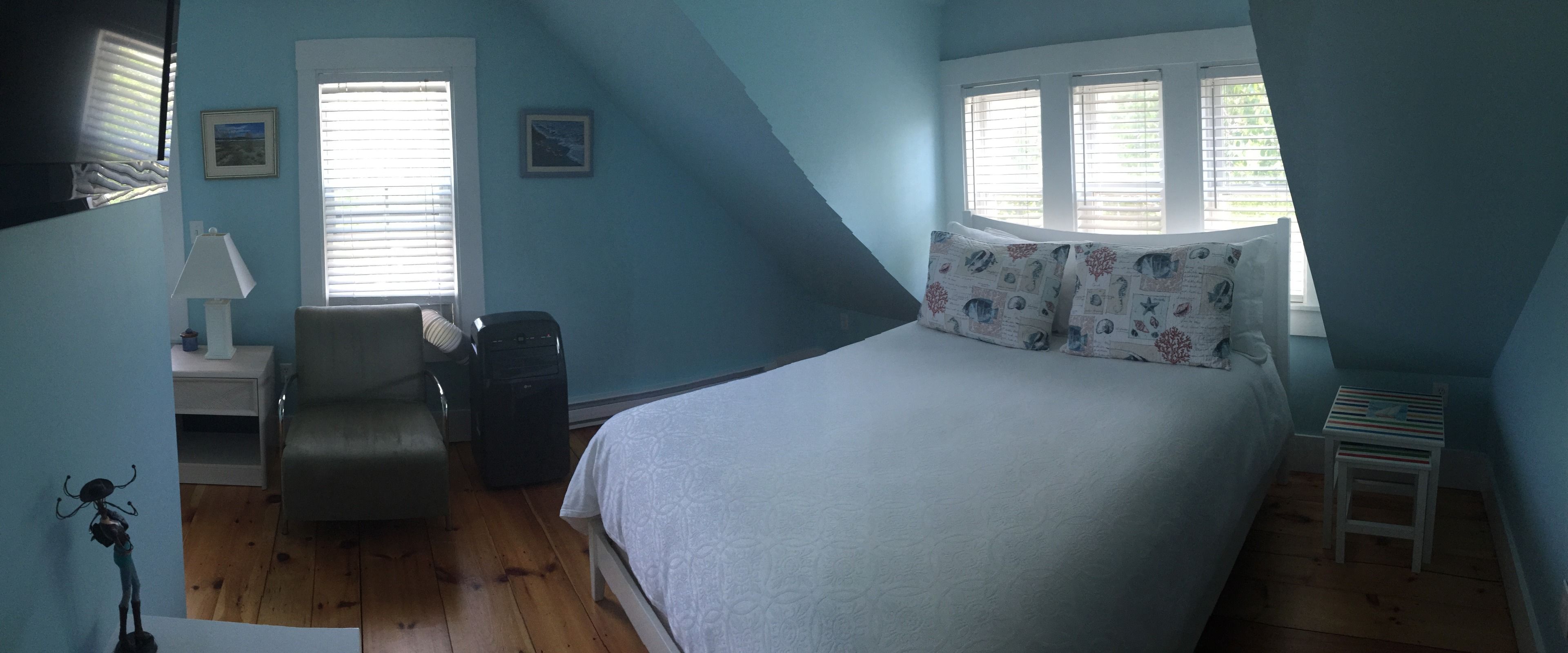 Un dormitorio con cama, una silla, una mesita de noche, una lámpara y una ventana con persianas.