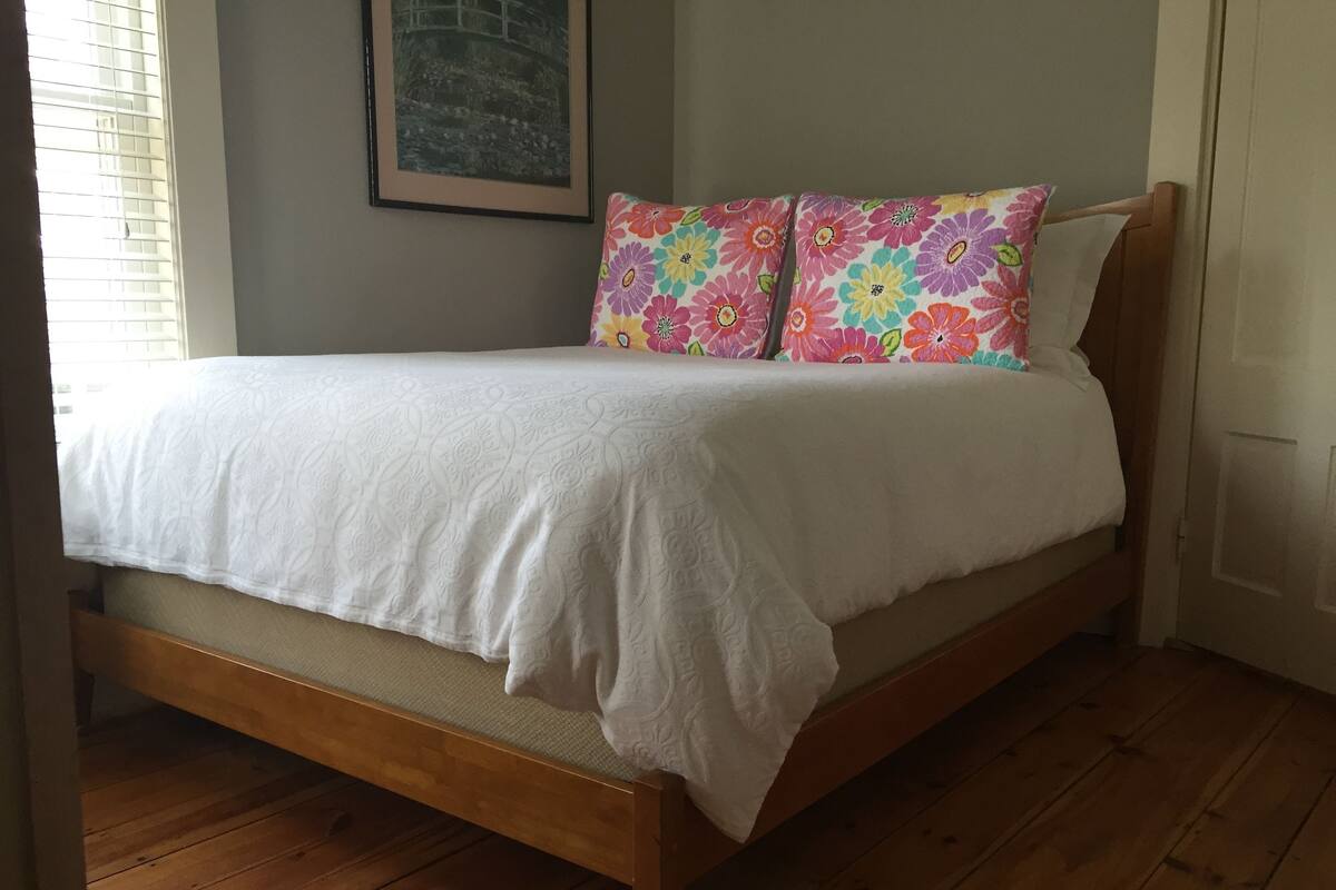 A wooden bed with a white bedspread and colorful floral pillows.