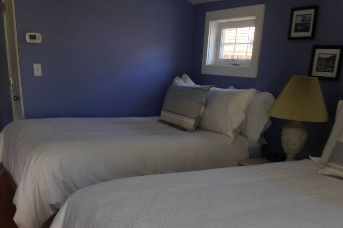 A bedroom with two beds, a window, and a lamp.