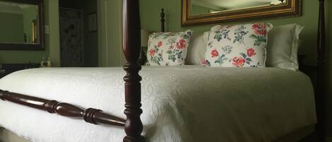 A four-poster bed with a white bedspread, floral pillows, and a mirror above.