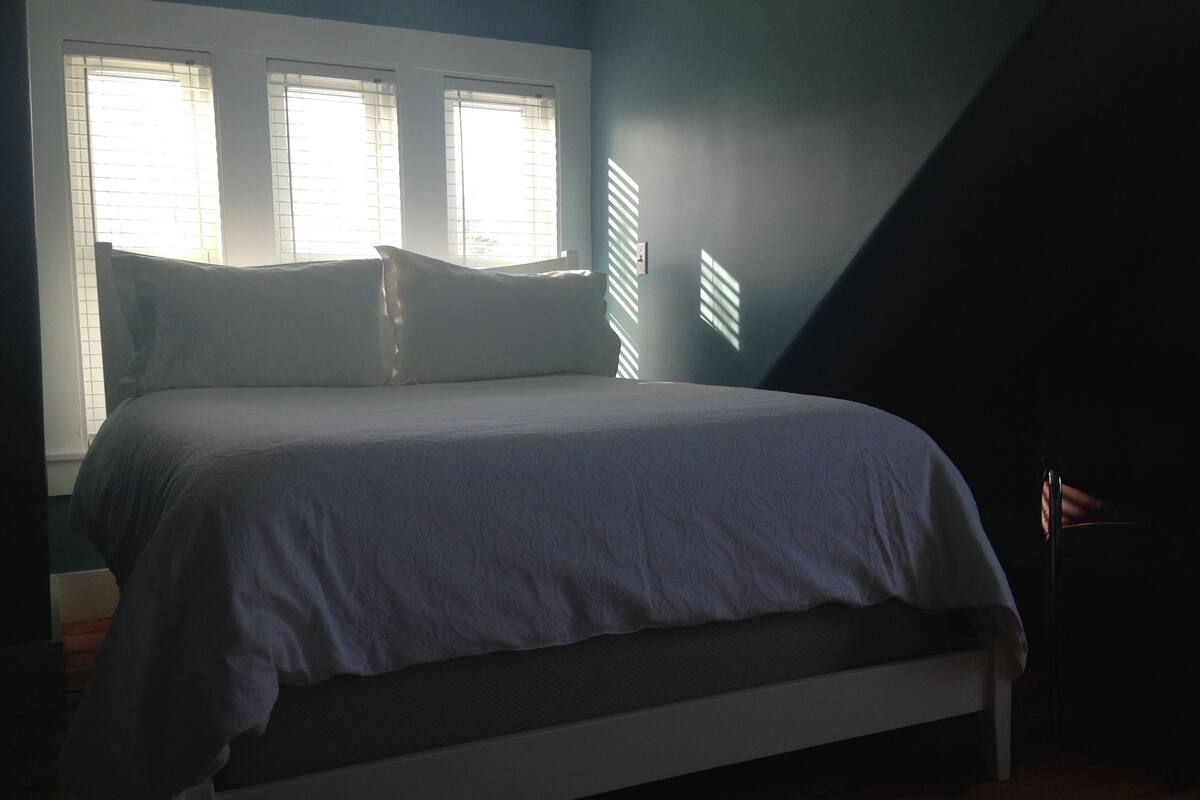 A bedroom with a bed, a nightstand, and a window with blinds.